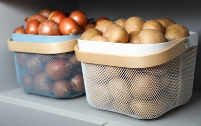 Baskets with potatoes and onions on shelf. Orderly storage