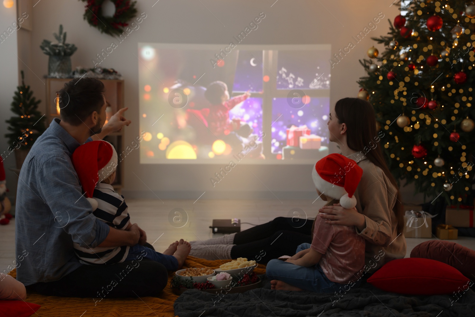 Photo of Family watching Christmas movie via video projector in cosy room. Winter holidays atmosphere