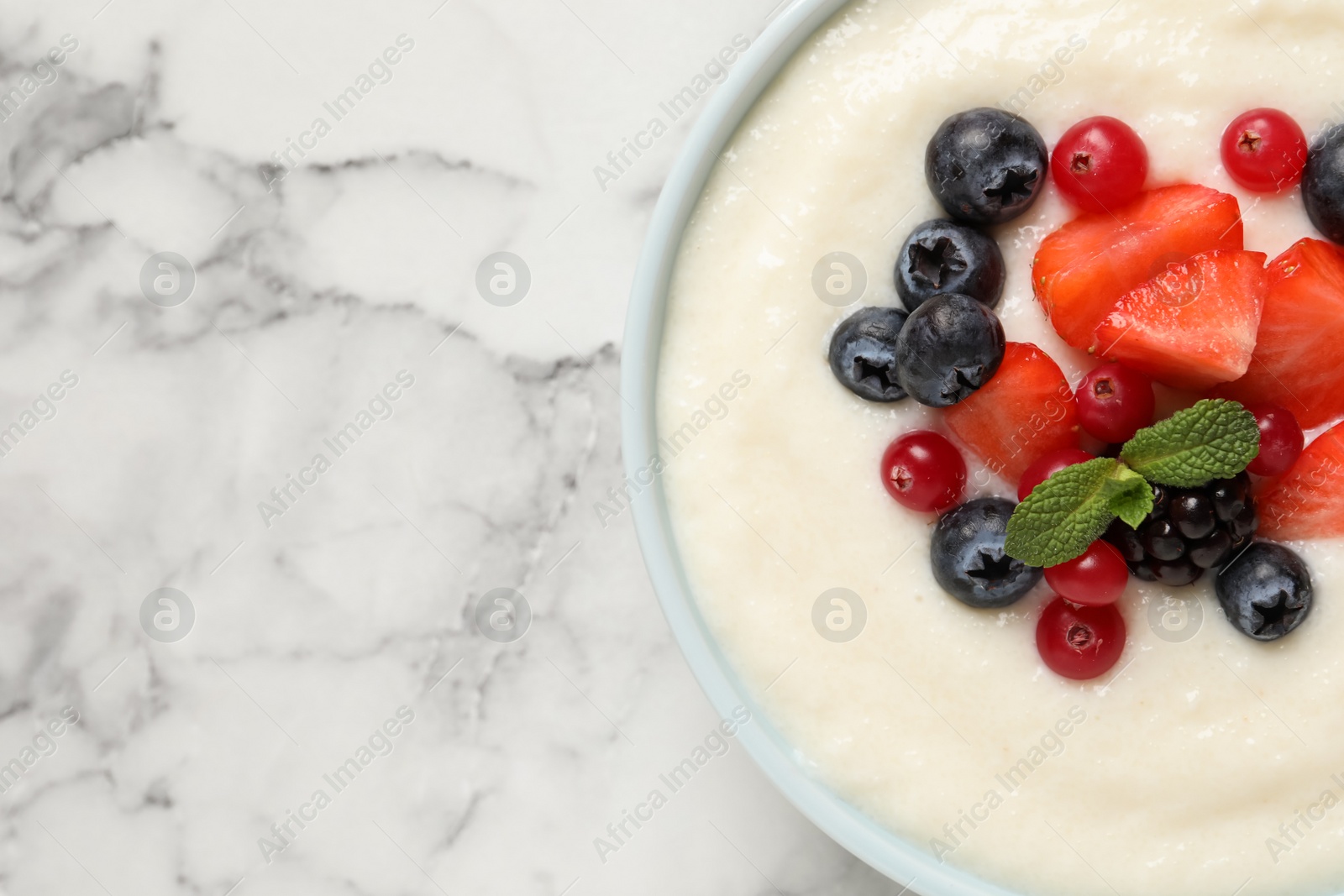 Photo of Delicious semolina pudding with berries on white marble table, top view. Space for text