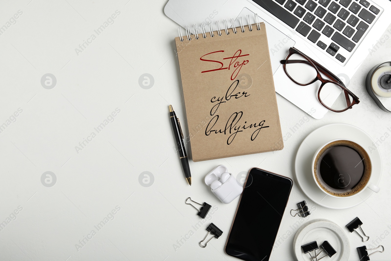 Image of Notebook with phrase STOP CYBER BULLYING, laptop and cup of coffee on white table, flat lay. Space for text