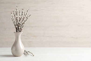 Photo of Beautiful pussy willow branches in vase on white wooden table, space for text