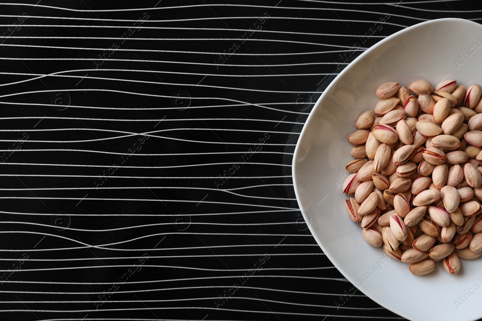 Photo of Many tasty pistachios on black table, top view. Space for text