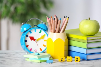 Photo of Alarm clock, apple and school stationery on white marble table