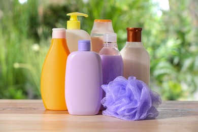 Different shower gel bottles and mesh pouf on wooden table