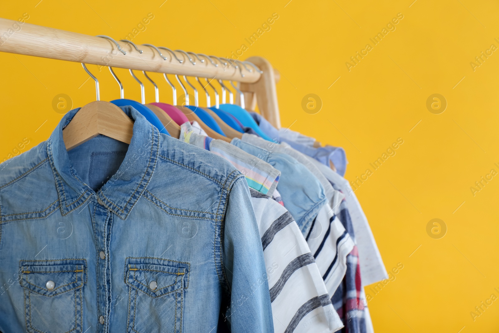 Photo of Rack with stylish children clothes on yellow background, closeup. Space for text