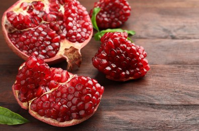 Cut fresh pomegranate and green leaves on wooden table, closeup. Space for text