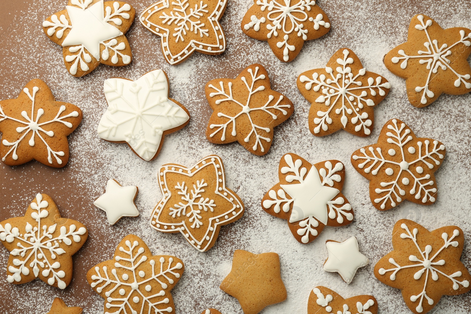 Photo of Tasty Christmas cookies with icing and powdered sugar on brown background, flat lay