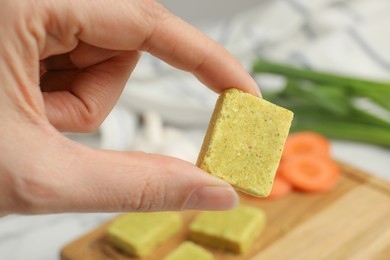 Photo of Woman holding bouillon cube over table, closeup