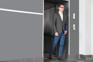 Photo of Young businessman walking out of modern elevator