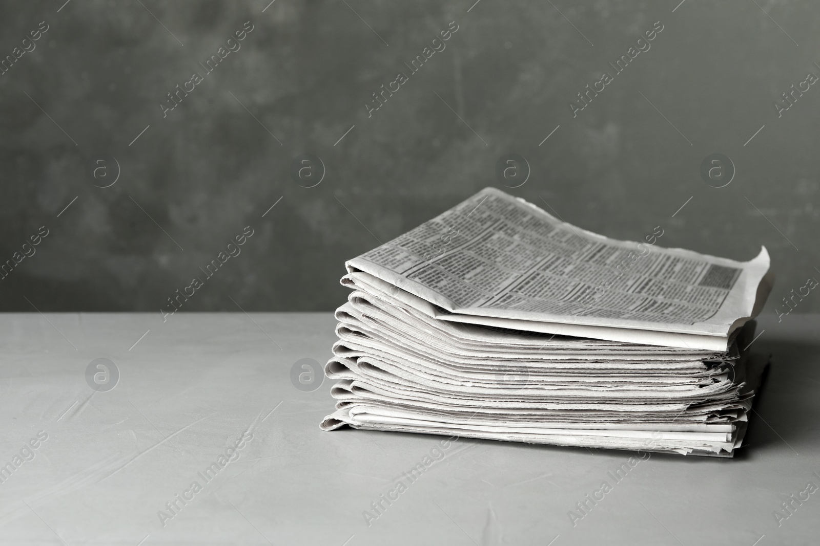 Photo of Stack of newspapers on light grey stone table, space for text. Journalist's work