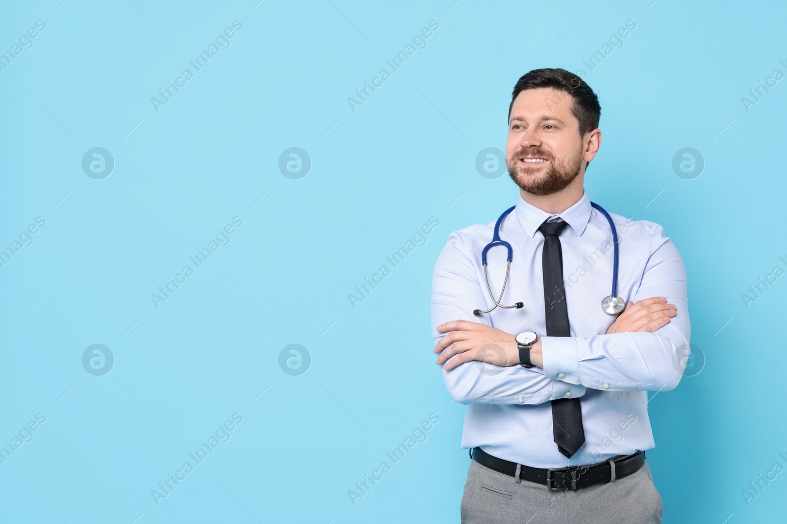 Photo of Smiling doctor with stethoscope on light blue background. Space for text