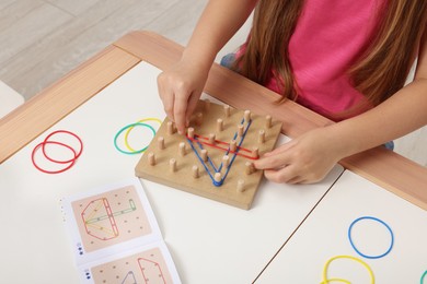 Motor skills development. Girl playing with geoboard and rubber bands at white table, closeup