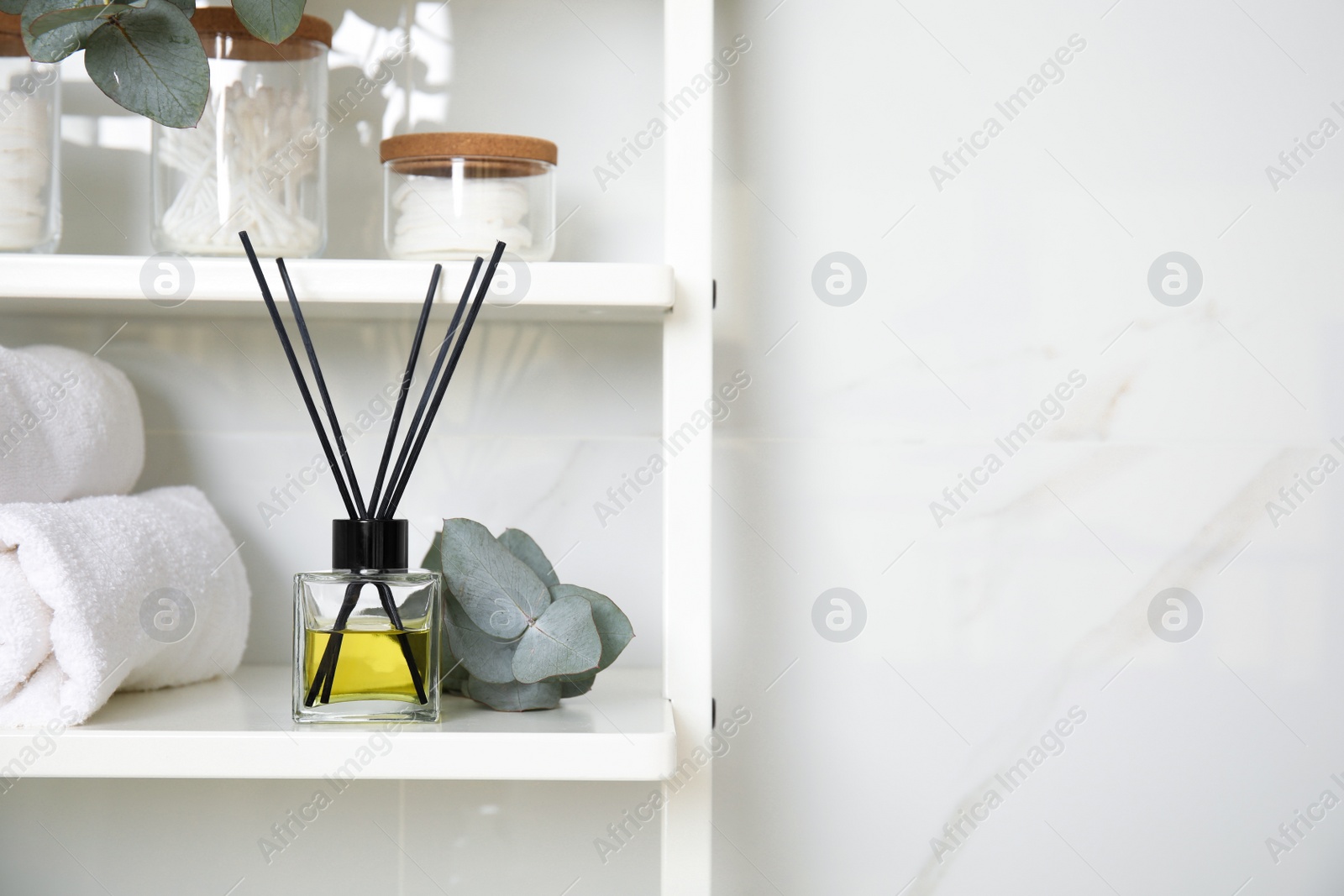 Photo of Aromatic reed air freshener, toiletries and rolled towels on white wooden shelf in bathroom. Space for text