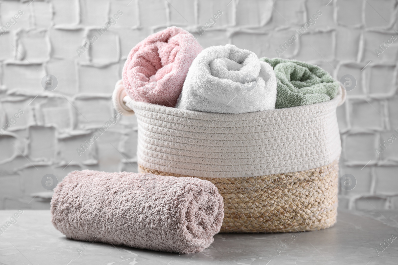 Photo of Rolled soft towels and wicker basket on grey table