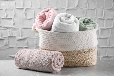 Photo of Rolled soft towels and wicker basket on grey table
