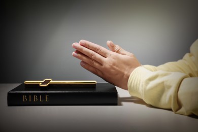 Image of Woman praying over Bible with cross at white table against grey background, closeup