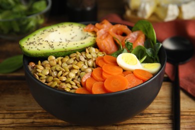 Photo of Delicious lentil bowl with carrot, avocado, egg and salmon on wooden table