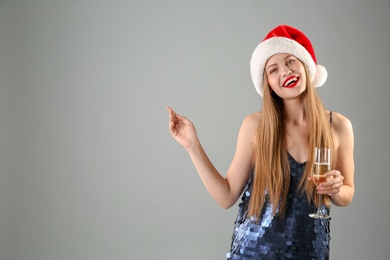 Photo of Young beautiful woman in Santa hat with glass of champagne on grey background. Christmas celebration