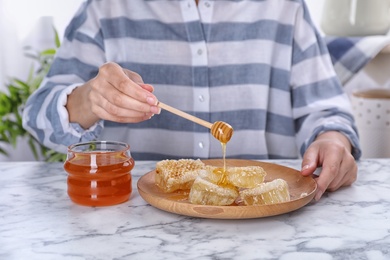 Photo of Woman pouring honey onto honeycombs at table