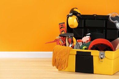 Photo of Box with different tools for repair on floor near orange wall, space for text