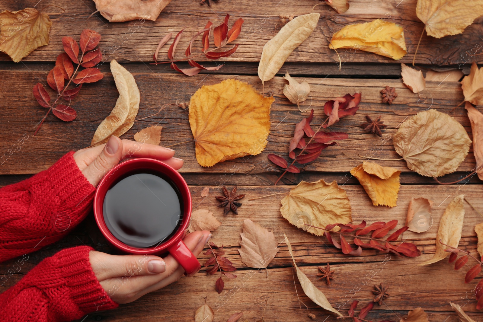 Photo of Woman with cup of hot drink at wooden table, top view. Cozy autumn atmosphere