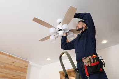 Photo of Electrician repairing ceiling fan with lamps indoors. Space for text