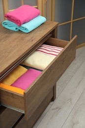 Wooden chest of drawers with different folded clothes indoors