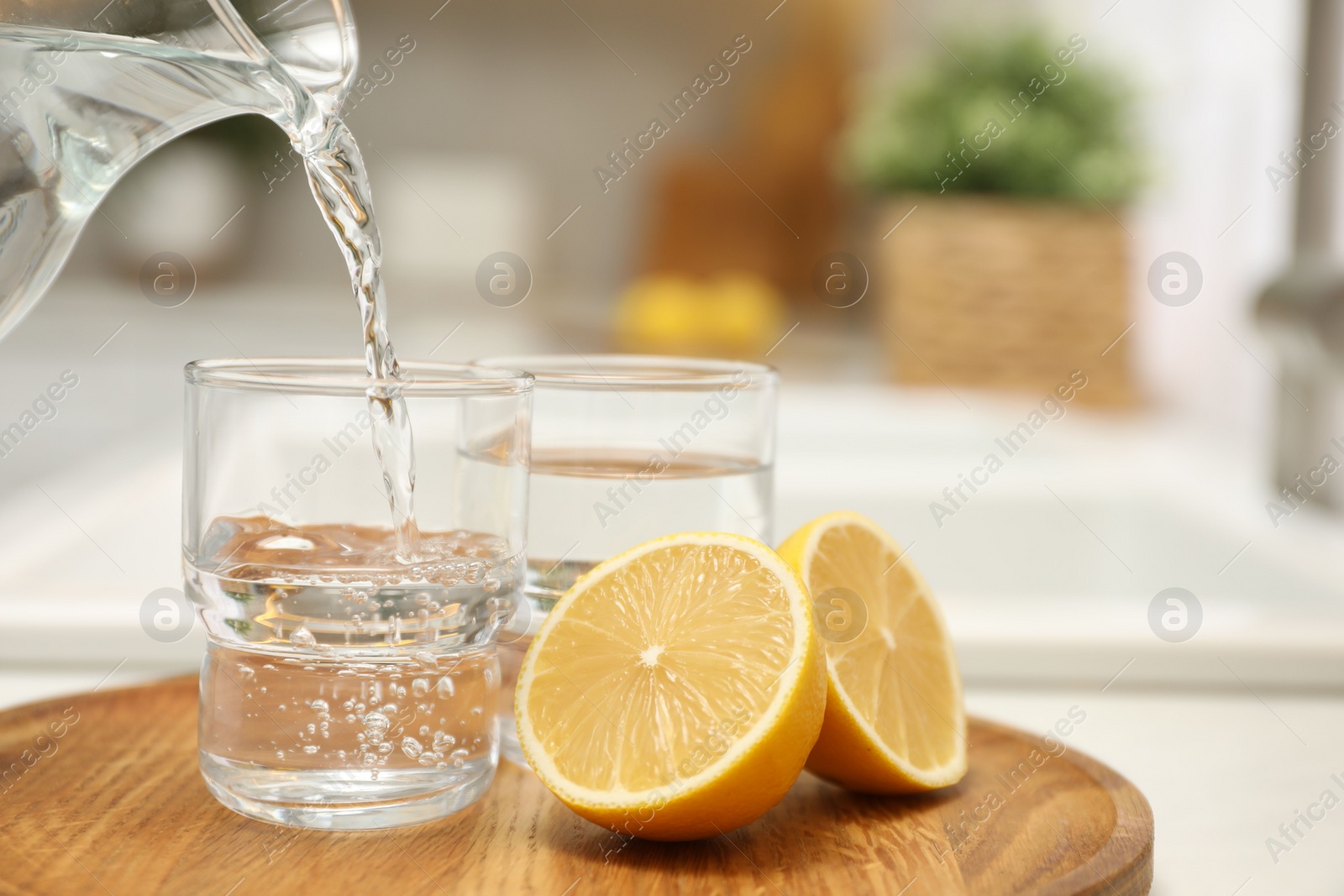 Photo of Pouring water from jug into glass on table in kitchen, closeup. Space for text