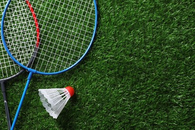 Photo of Two badminton rackets and shuttlecock on green grass, top view with space for text