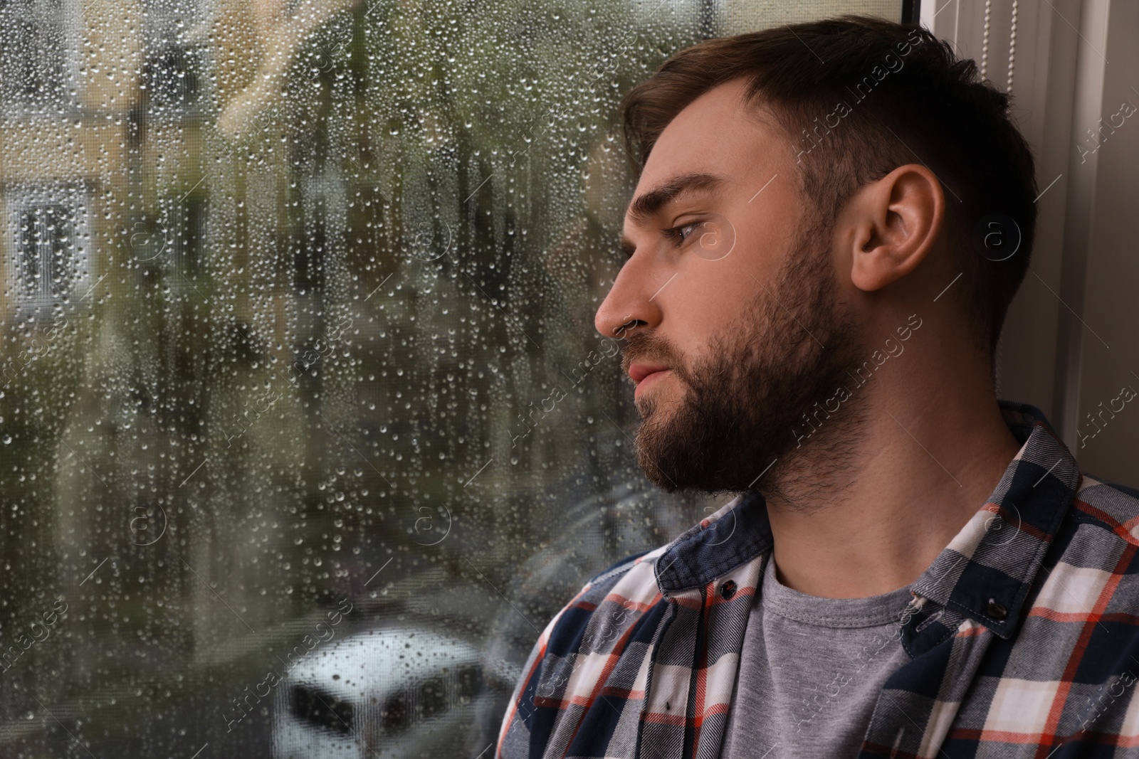 Photo of Depressed man near window at home. Space for text