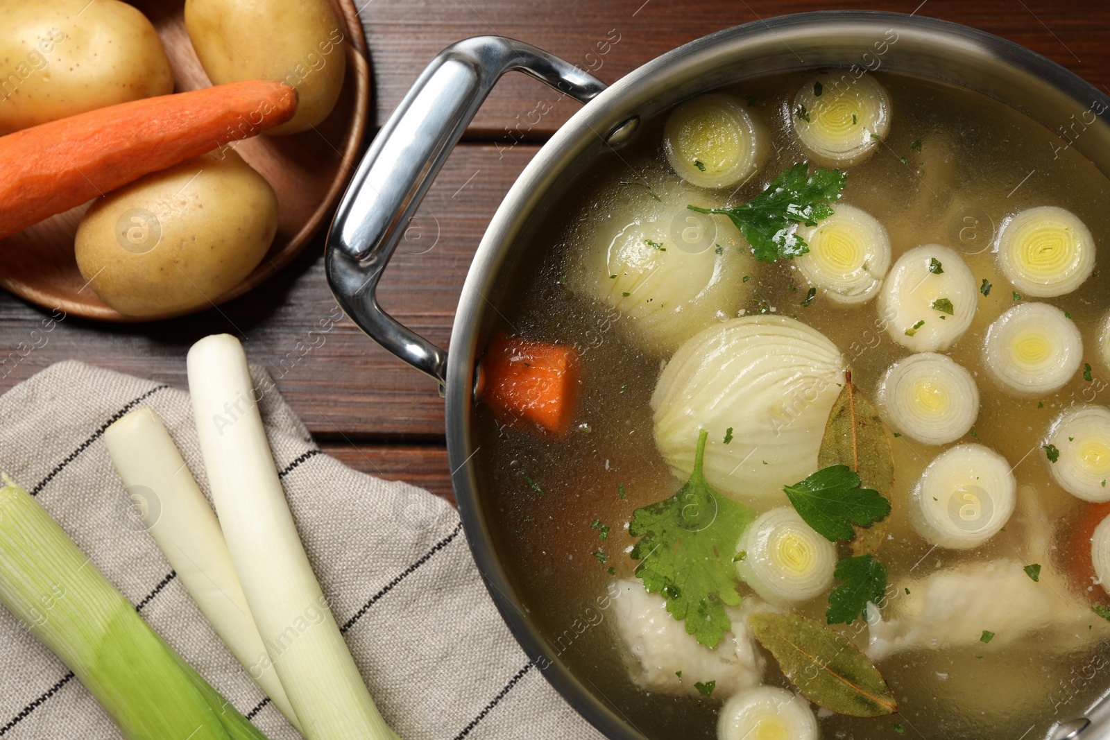 Photo of Pot with tasty bouillon and different ingredients on wooden table, flat lay