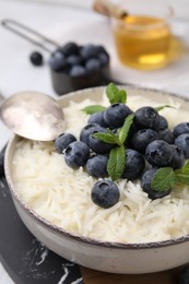 Photo of Bowl of delicious rice porridge with blueberries and mint on table, closeup