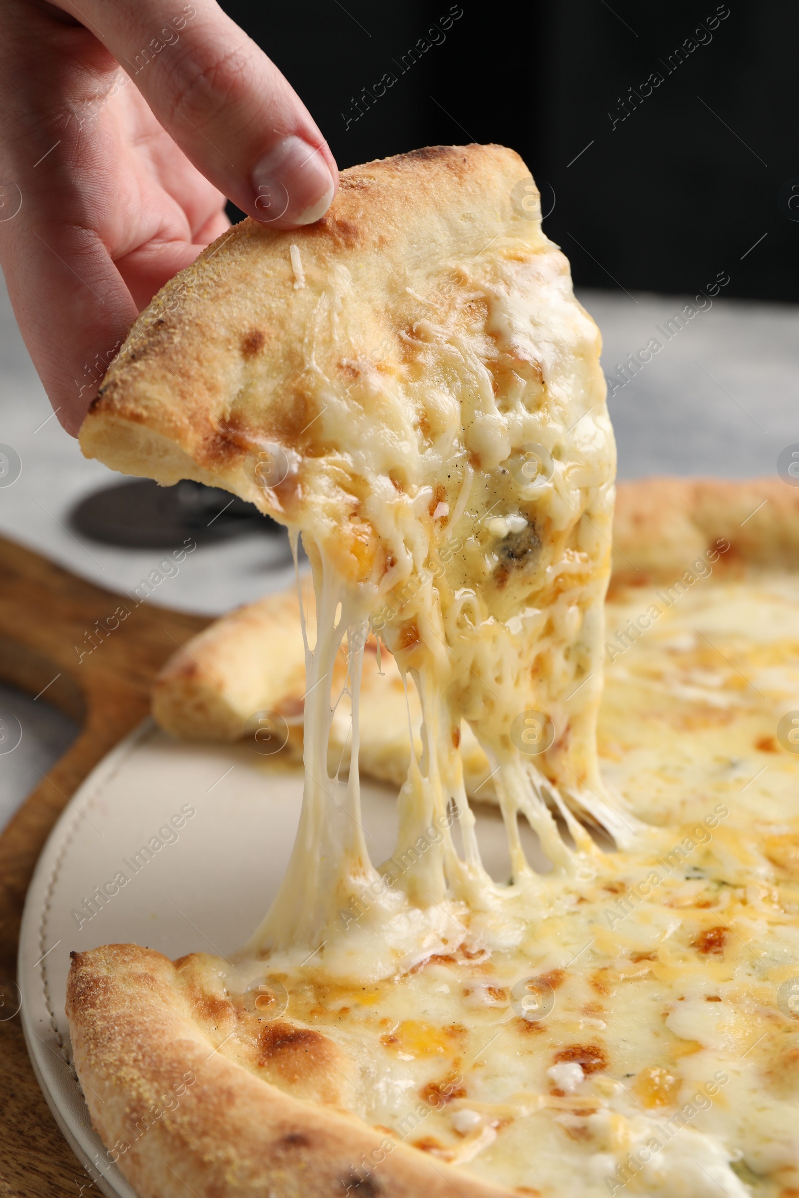 Photo of Woman taking piece of delicious cheese pizza at table, closeup