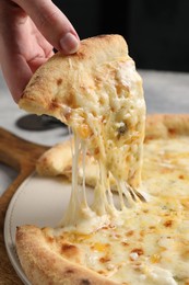 Woman taking piece of delicious cheese pizza at table, closeup