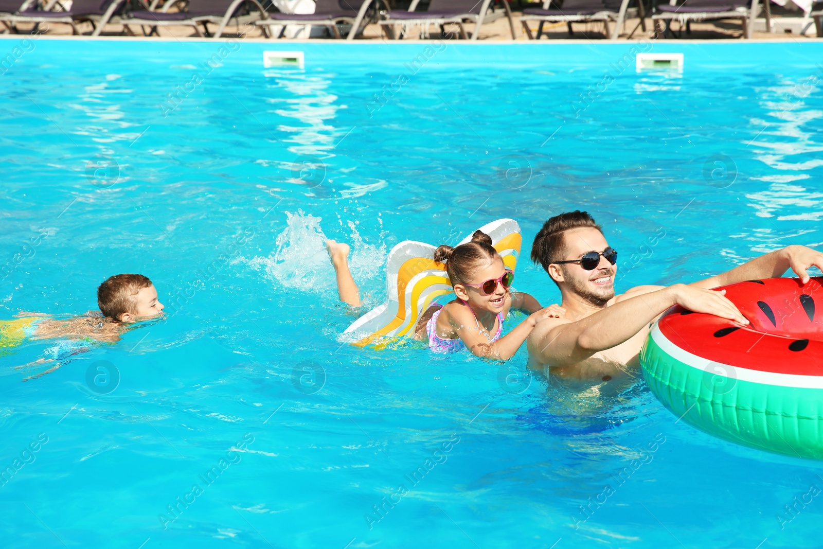 Photo of Young father with little children in swimming pool on sunny day