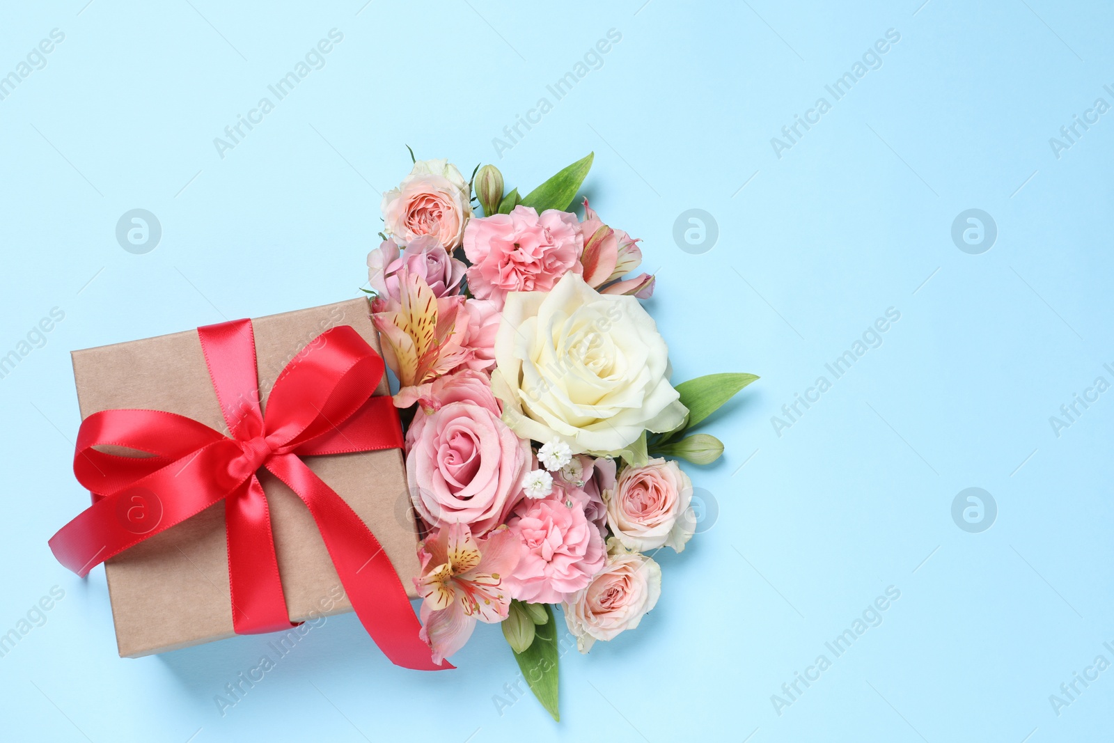 Photo of Gift box and beautiful flowers on light blue background, flat lay. Space for text