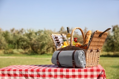 Photo of Picnic basket with wine, snacks and mat on table in park. Space for text