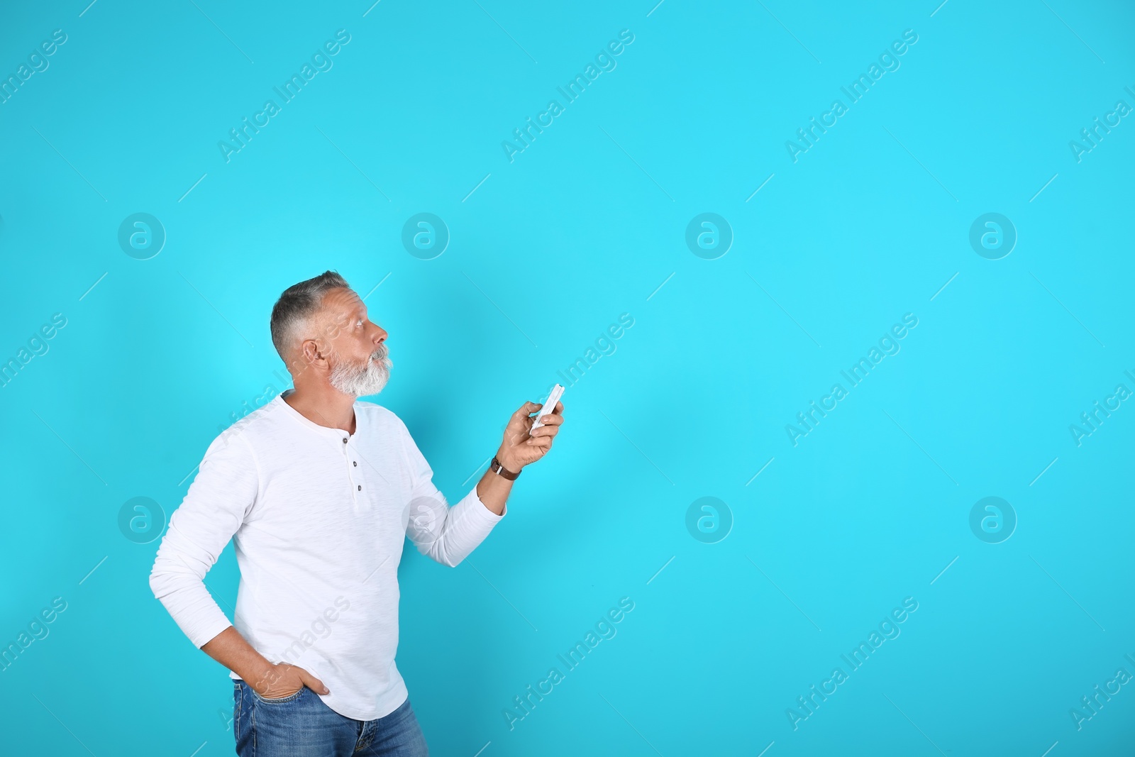 Photo of Senior man with air conditioner remote control on color background