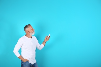 Photo of Senior man with air conditioner remote control on color background