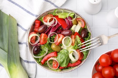 Bowl of tasty salad with leek and olives served on white tiled table, flat lay