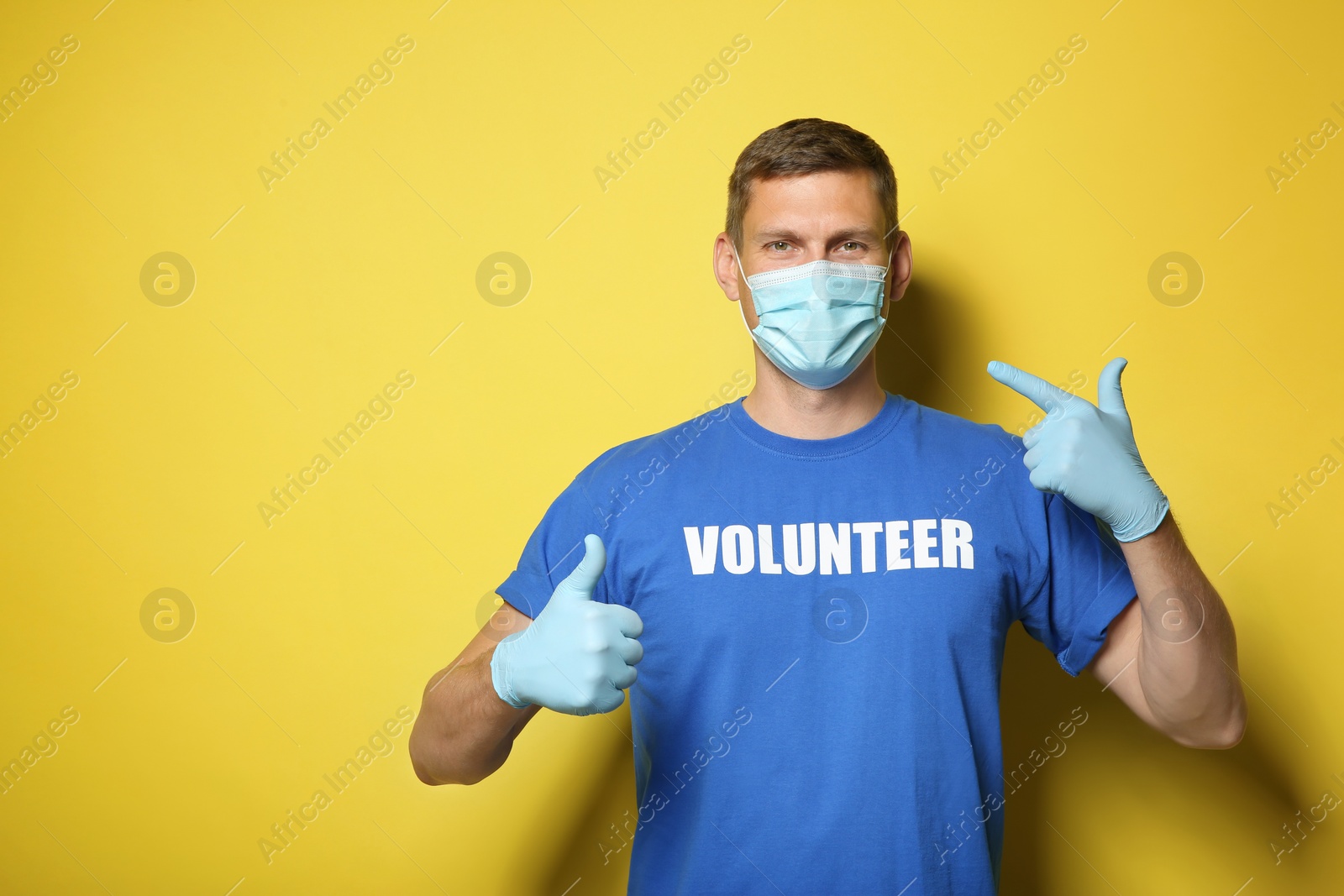Photo of Male volunteer in mask and gloves on yellow background, space for text. Protective measures during coronavirus quarantine