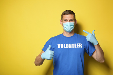 Photo of Male volunteer in mask and gloves on yellow background, space for text. Protective measures during coronavirus quarantine