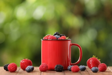 Photo of Mug with different fresh ripe berries on wooden table outdoors