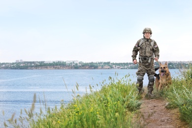 Photo of Man in military uniform with German shepherd dog near river