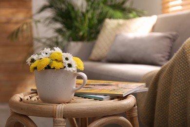 Photo of Cup with beautiful bright flowers on table in living room, space for text