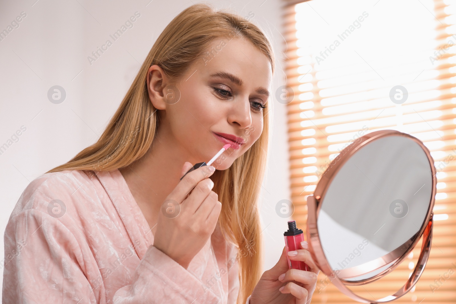 Photo of Beautiful happy woman applying makeup in room