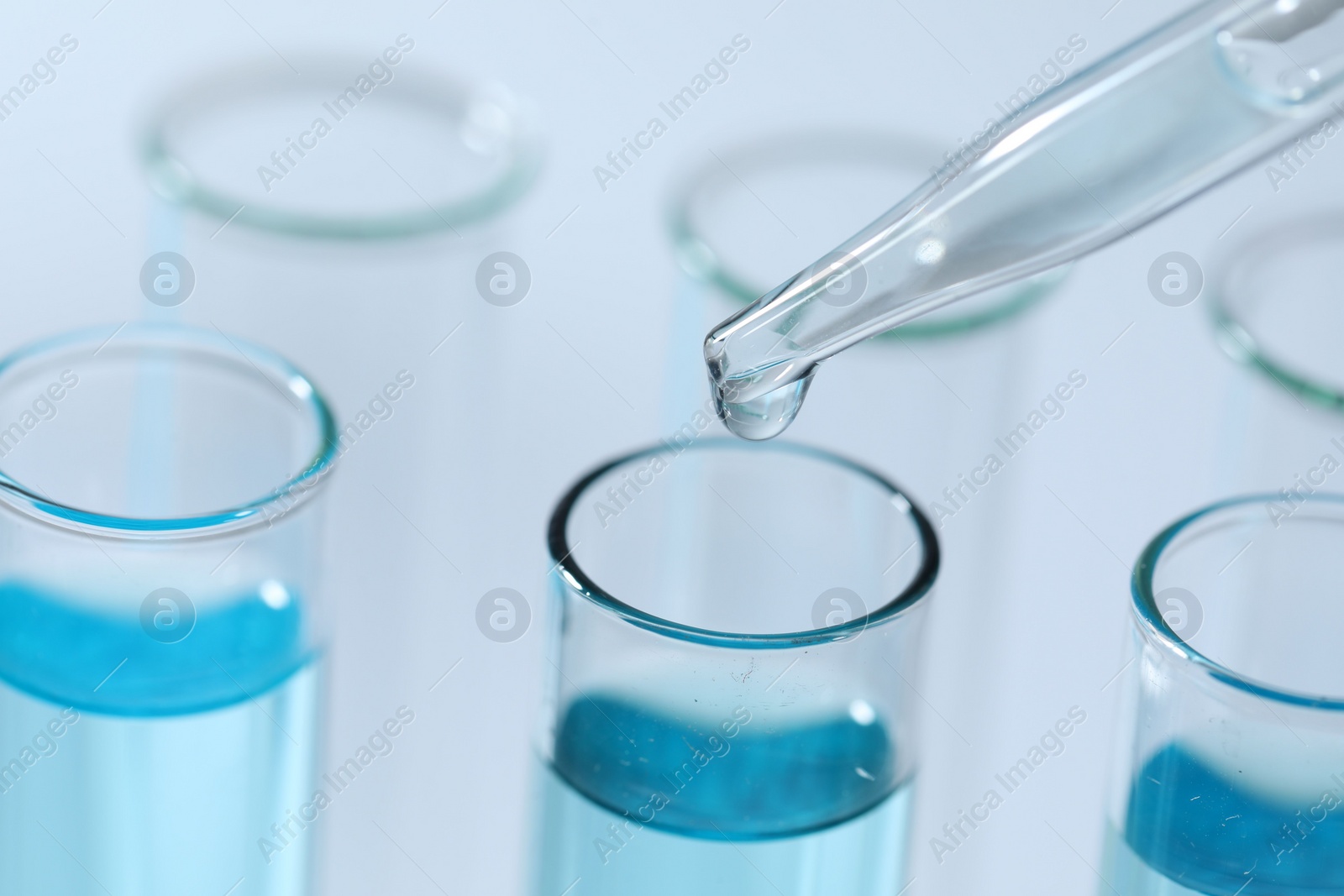 Photo of Dripping liquid from pipette into test tube on light background, closeup