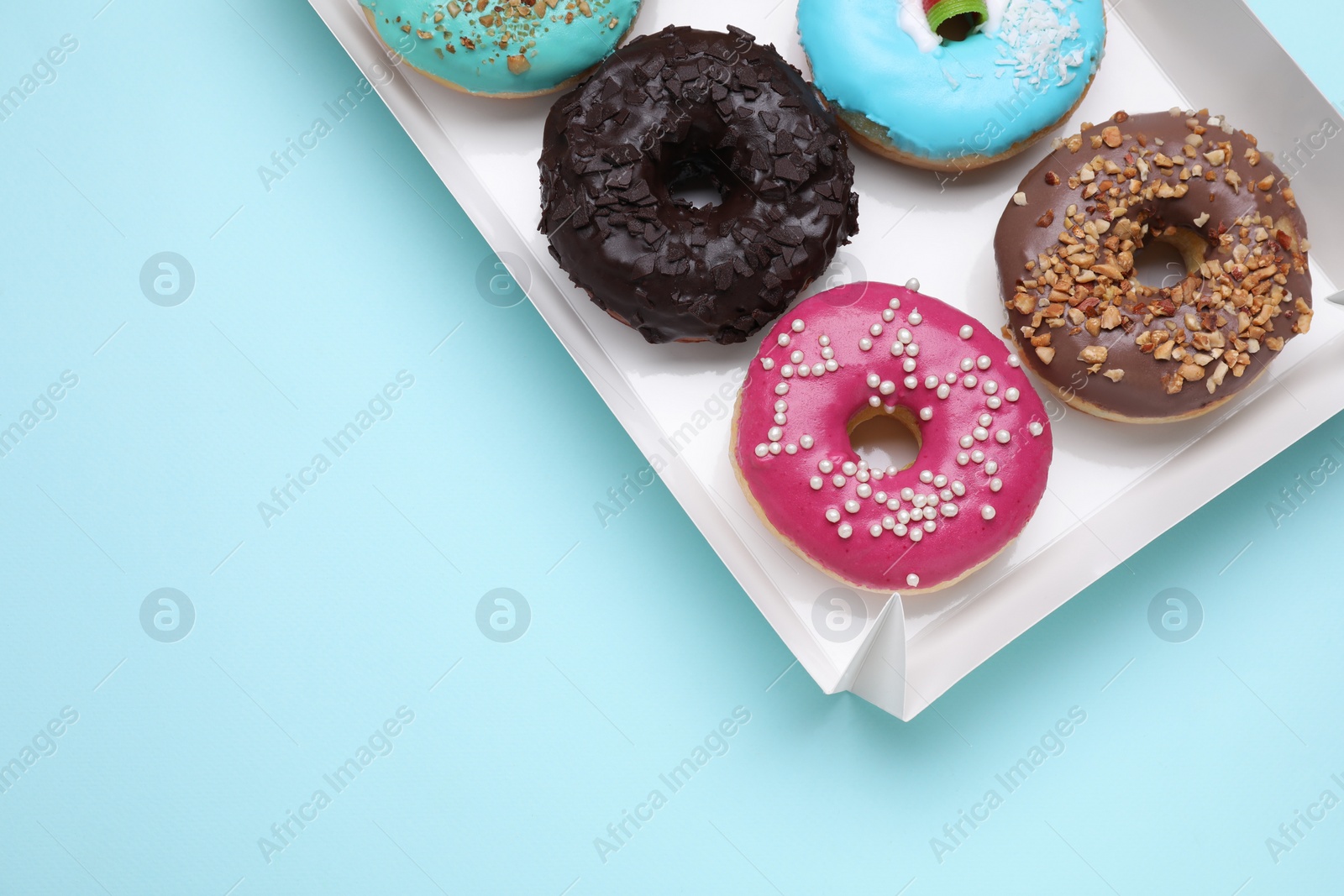 Photo of Box with different tasty glazed donuts on light blue background, top view. Space for text