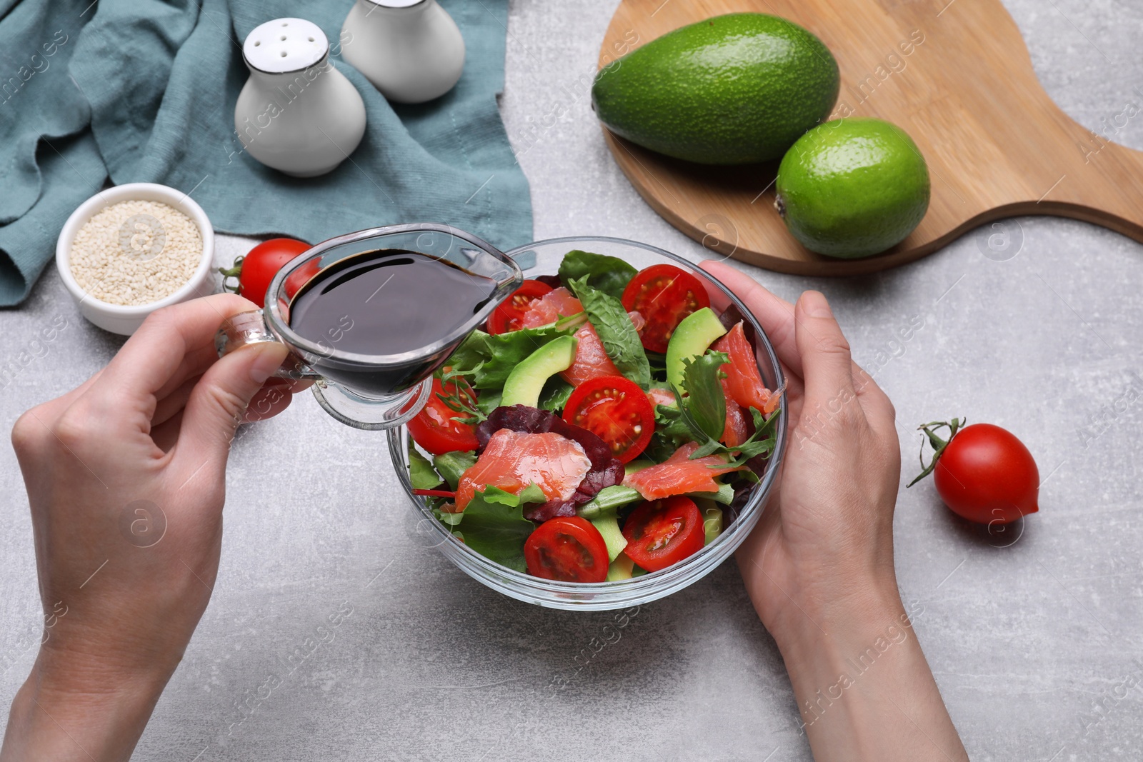 Photo of Woman adding soy sauce to tasty salad at grey table, closeup