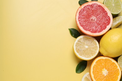 Different cut and whole citrus fruits on yellow table, flat lay. Space for text